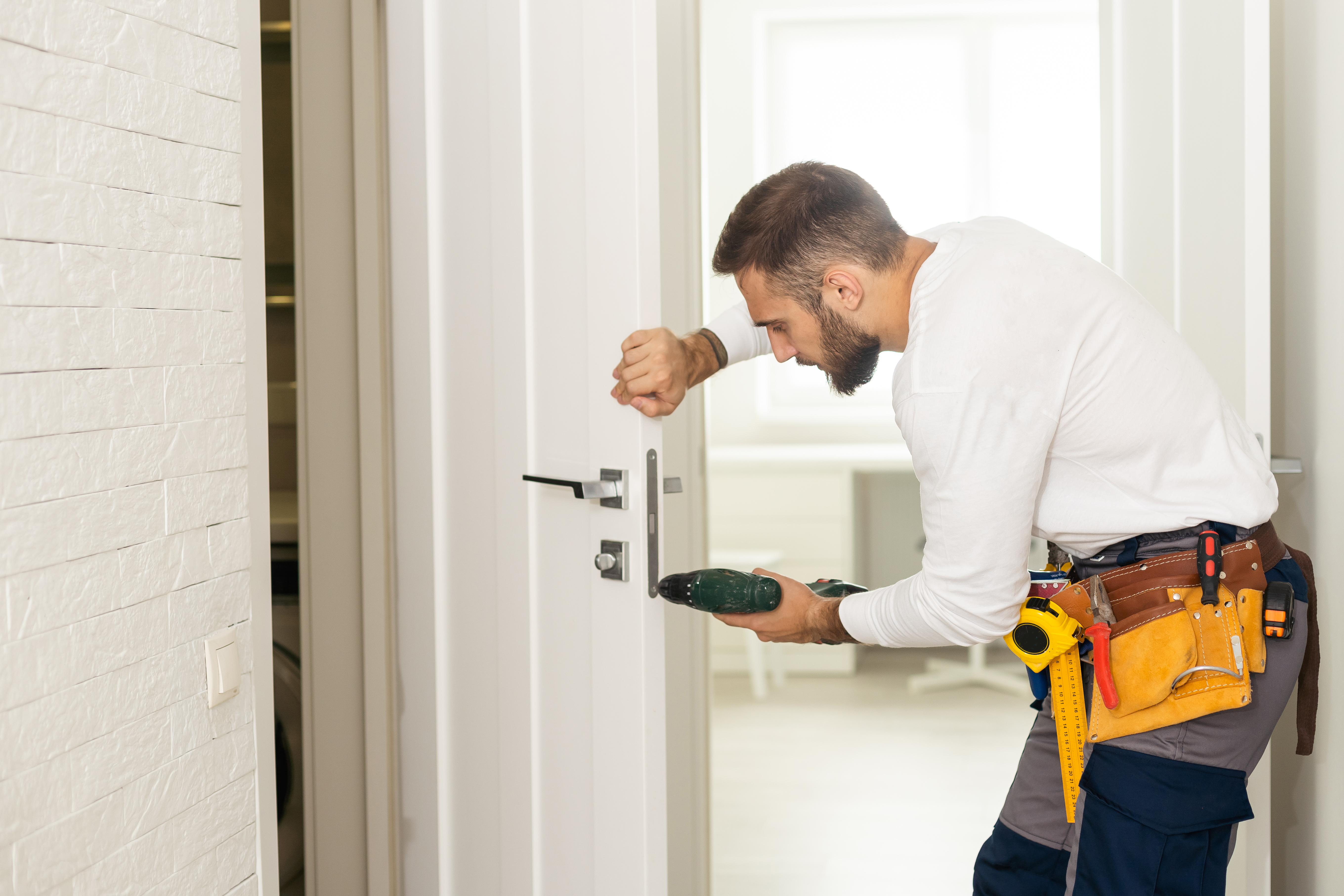 good looking man working as handyman and fixing a door lock in a house entrance.