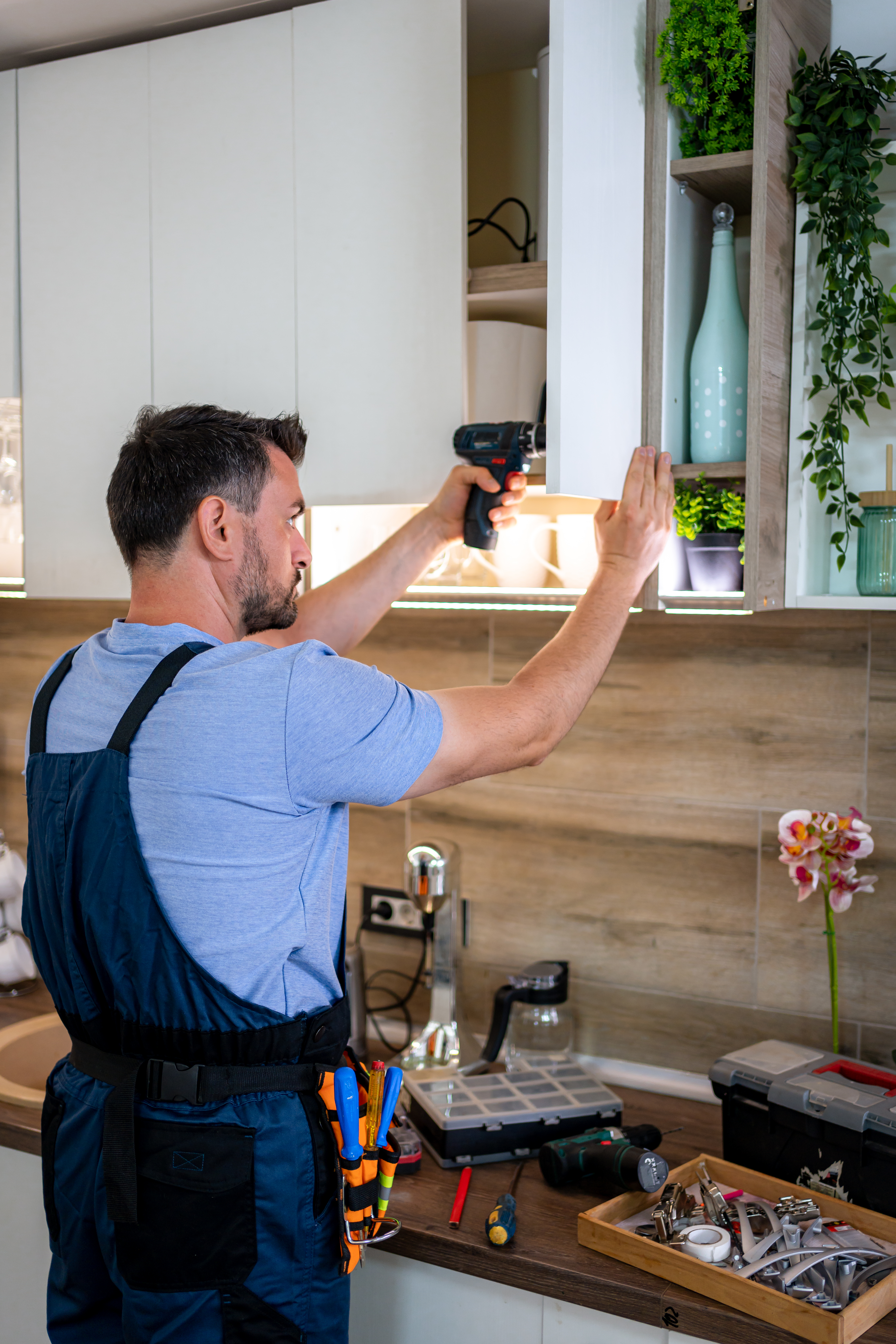 Craftsman uses a power tool to install kitchen cabinets while organizing his workspace.